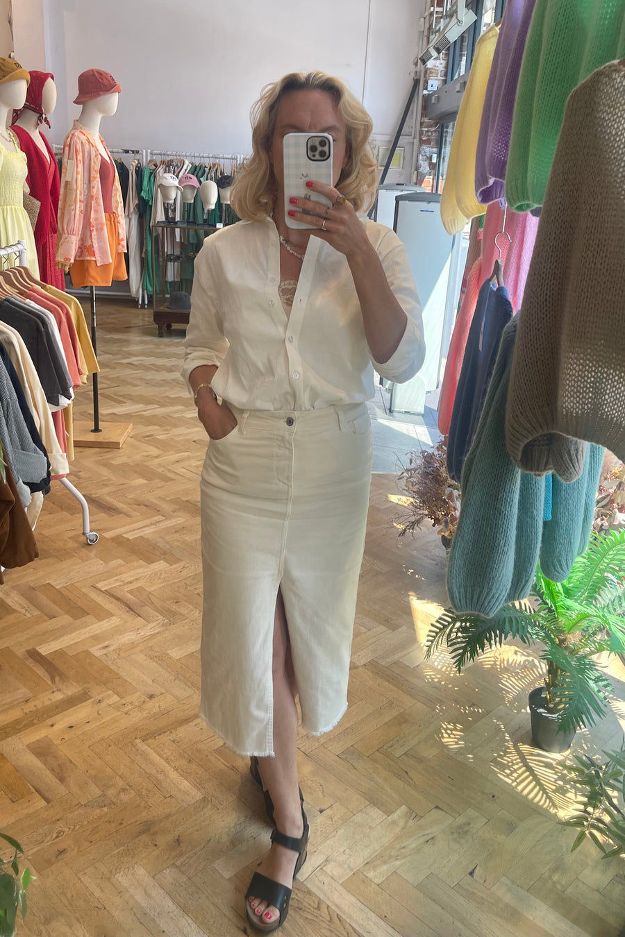 Woman in boutique wearing long white denim skirt, cotton button up shirt, and black summer sandals